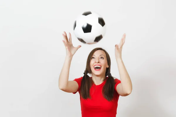 Active European young woman, two fun pony tails, football fan or player in red uniform catching classic soccer ball isolated on white background. Sport play football health, healthy lifestyle concept.