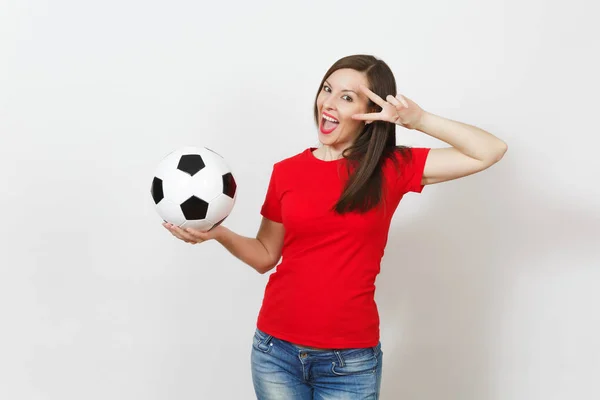 Pretty European young woman, football fan or player in red uniform holding classic soccer ball, fingers near eye isolated on white background. Sport, play football, health, healthy lifestyle concept.