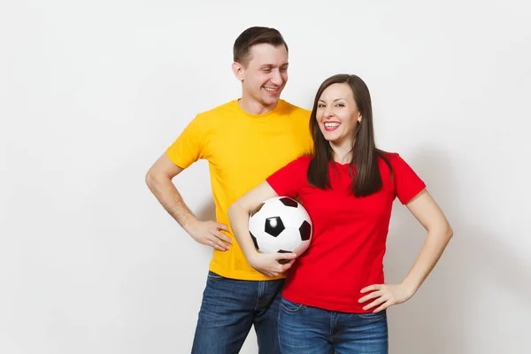 Весела усміхнена весела молода пара, жінка, чоловік, шанувальники футболу в жовтій і червоній формі підбадьорюють команду підтримки, що тримає футбольний м'яч ізольовано на білому тлі. Спорт, сімейне дозвілля, концепція способу життя . — стокове фото