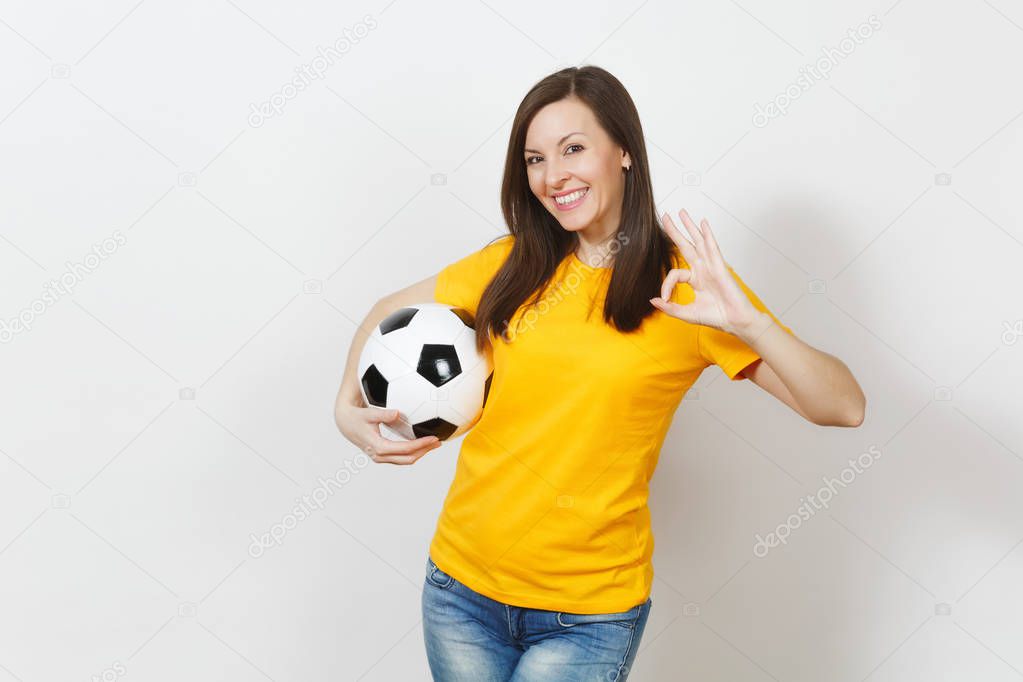 Beautiful European young woman, football fan or player in yellow uniform holding soccer ball showing OK gesture isolated on white background. Sport, play football, health, healthy lifestyle concept.