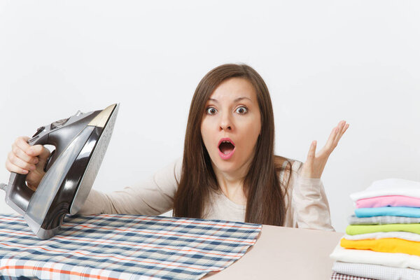 Close up fun tired shocked housewife in light clothes ironing checkered shirt, clothing on ironing board with iron. Woman isolated on white background. Housekeeping concept. Copy space advertisement.