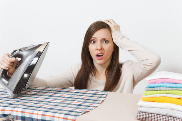 Close up fun tired shocked housewife in light clothes ironing checkered shirt, clothing on ironing board with iron. Woman isolated on white background. Housekeeping concept. Copy space advertisement.