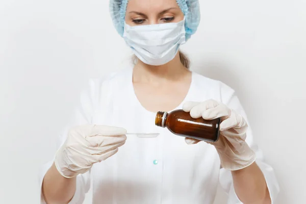 Medico donna in maschera viso, cappello sterile, guanti versare medicina liquida in cucchiaio da bottiglia isolata su sfondo bianco. Medico donna in abito medico. Personale sanitario, salute, concetto di medicina . — Foto Stock