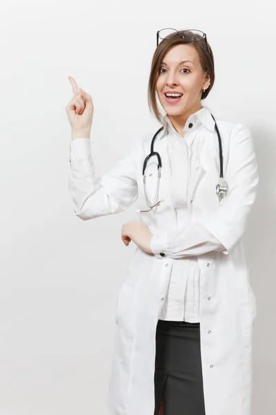 Giovane donna medico sorridente con stetoscopio, occhiali isolati su sfondo bianco. Medico donna in abito medico indicando indice da parte sullo spazio copia. Concetto di medicina sanitaria del personale sanitario — Foto Stock
