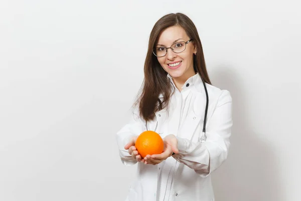 Sonriendo feliz atractiva joven doctora mujer con estetoscopio, gafas aisladas sobre fondo blanco. Doctora en bata médica sosteniendo naranja. Personal sanitario, salud, concepto de medicina . — Foto de Stock