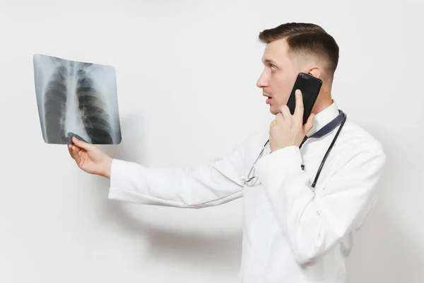 Doctor enfocado hombre con rayos X de pulmones, fluorografía, roentgen, hablando por teléfono móvil aislado sobre fondo blanco. Médico en uniforme médico, estetoscopio. Personal sanitario. Neumonía . — Foto de Stock