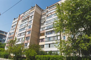 Yeşil ağaçlar ve çalılar açık mavi gökyüzü arka plan üzerinde çevrili çok katlı yüksek katlı Sovyetler-ev inşa cephe. Mimari, tarihi