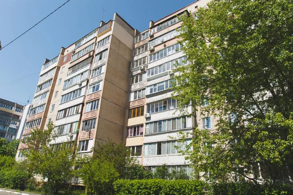 Die Fassade eines mehrstöckigen sowjetisch erbauten Hochhauses, umgeben von grünen Bäumen und Büschen vor klarem blauen Himmel. Architektur, Geschichte — Stockfoto