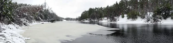 Panorama Beautiful natural landscape. Half frozen and ice-covered winter wide river in the forest with coniferous trees, bushes and snow drifts on the both banks — Stock Photo, Image