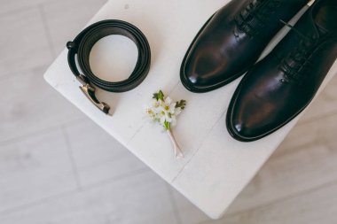 Arka plan üzerinde bir sandalyeye damat için güzel şık düğün cilalı ayakkabı bağlarına siyah ayakkabılarla, kemer ve çiçek yaka çiçeği kadar hafif bir ahşap zemin kapatın. Düğün giyim, Aksesuar