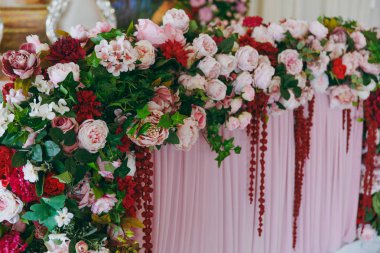 Güzel dekorasyon düğün Ziyafet pembe, Bordo ve beyaz tonlarda tentenin altında. Yeni evliler, büyük çiçek düzenleme gül, peonies ve yeşil yaprakları ile süslenmiş Ziyafet masa