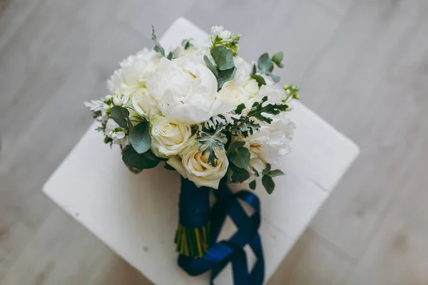 Gros plan Un beau bouquet de mariée tendre aux couleurs pastel de roses, pivoines et brindilles vertes nouées d'un long ruban bleu soie sur fond d'une chaise en bois. Accessoires de mariage pour mariée — Photo
