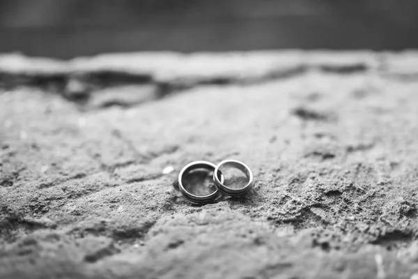 Fechar Dois belos anéis de casamento largos elegantes com tiras da noiva e noivo cruzam-se em um fundo cinza áspero de pedra. Acessórios de casamento, jóias — Fotografia de Stock