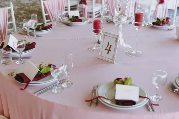 Bela decoração do banquete de casamento sob o toldo em tons rosa, borgonha e branco. Cenário de mesa em um salão com pratos, talheres, copos, guardanapos e cartões, composições florais decoradas — Fotografia de Stock