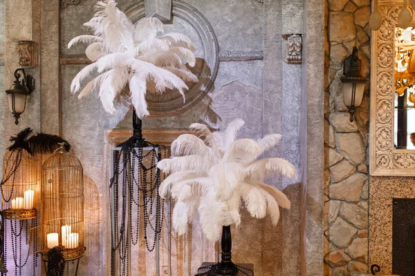 Hermosa decoración de un lujoso banquete de bodas en un restaurante de estilo retro. Elementos de decoración Grandes composiciones de plumas blancas y jaulas para pájaros con velas y perlas en un interior vintage — Foto de Stock