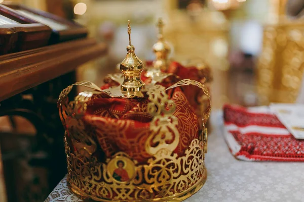 Ślub w cerkwi. Dwa uroczyste korony i ręcznik haftowany czerwony i czarny wątku na stół z białym obrusem w pobliżu ikonostas na tle wnętrze kościoła — Zdjęcie stockowe