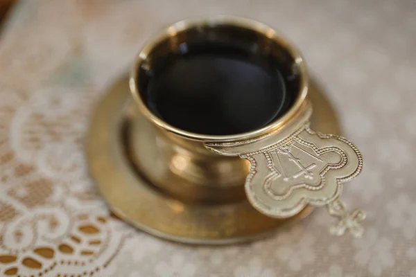 Wedding in the Orthodox Church. Elements of the interior design of the church A golden cup with holy water, decorated with a crown with a cross on a saucer on a white tablecloth — Stock Photo, Image