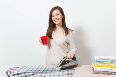 Kırmızı fincan çay veya kahve, Ütü gömlek, giyim demir ile Ütü Masası üzerine ışık giysili genç ev hanımı. Beyaz arka plan üzerinde izole kadın. Temizlik kavramı. Kopyalama alanı reklam.