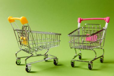 İki süpermarket bakkal itme at arabası tekerlekler ile alışveriş ve üzerinde yeşil arka plan izole kolu üzerinde plastik öğeleri sarı ve pembe yakın çekim. Alışveriş kavramı. Kopya alanı reklam için