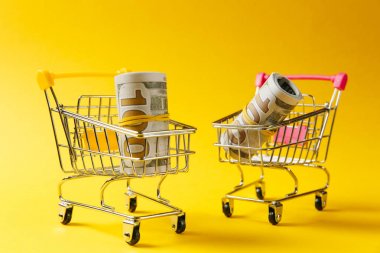 Sarı arka plan üzerinde izole dolar demetleri ile sarı ve pembe saplı alışveriş için iki süpermarket bakkal itme at arabası kapatın. Alışveriş kavramı. Kopya alanı reklam için