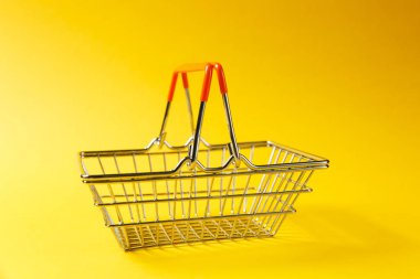 Metal alışveriş sepetinin kaldırdı kolları ve Sarı zemin üzerine izole turuncu plastik elemanları süpermarkette alışveriş için kapatın. Alışveriş kavramı. Kopya alanı reklam için