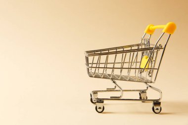 Süpermarket bakkal itme sepetinin siyah jantlar ve tutamacı üzerinde bej arka plan izole sarı plastik öğelerle birlikte alışveriş için kapatın. Alışveriş kavramı. Kopya alanı reklam için