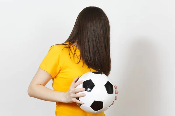 Beautiful European young woman, football fan or player in yellow uniform hold soccer ball, cover face with hair isolated on white background. Sport, play football, health, healthy lifestyle concept.