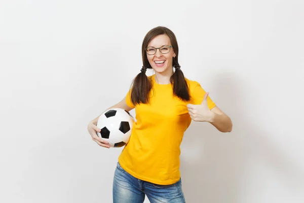 Donna europea sorridente, due divertenti code di cavallo, tifoso di calcio o giocatore in occhiali, pollice giallo uniforme spettacolo su, tenere il pallone da calcio isolato su sfondo bianco. Sport, calcio, stile di vita sano . — Foto Stock