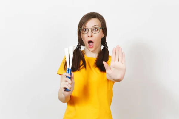 Beautiful European young woman with fun pony tails, fan or player in glasses, yellow uniform show stop gesture, hold football pipe isolated on white background. Sport fan, healthy lifestyle concept. — Stock Photo, Image