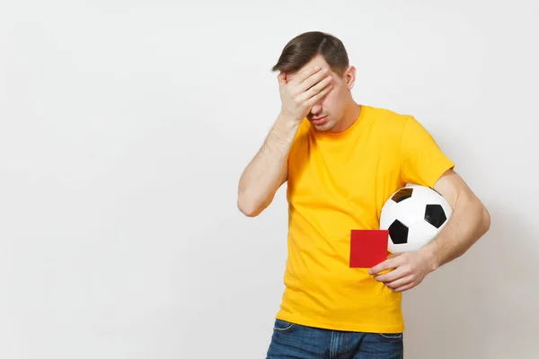 Triste sconvolto piangendo scioccato giovane uomo, tifoso di calcio o giocatore in uniforme gialla coprire gli occhi a mano, tenere cartellino rosso per ritirarsi dal campo isolato su sfondo bianco. Sport gioco, stile di vita concetto . — Foto Stock