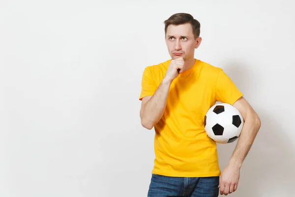 Ispirato giovane pensoso uomo europeo, tifoso o giocatore in uniforme gialla tenere palla da calcio, tifo squadra di calcio preferita isolata su sfondo bianco. Sport, calcio, stile di vita sano . — Foto Stock