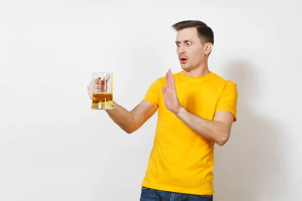 Young European serious handsome man in yellow t-shirt refuse pint mug of beer, show stop drink alcohol gesture with hand isolated on white background. Sport teenager health, healthy lifestyle concept. — Stock Photo, Image