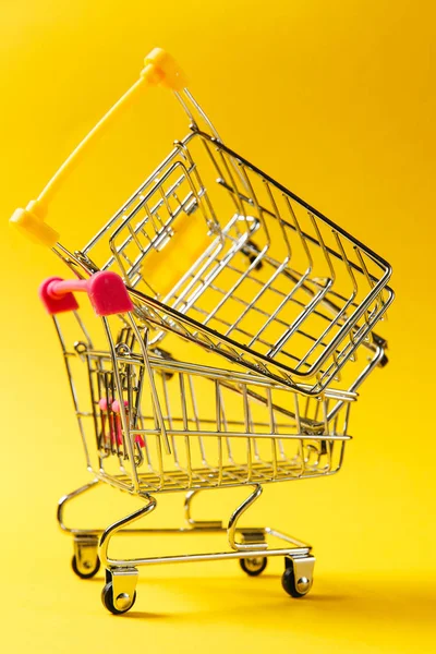 Κοντινό πλάνο της δύο σούπερ μάρκετ παντοπωλείο ώθησης κάρρα για ψώνια με κίτρινες και ροζ στοιχεία στη λαβή σε κάθε άλλο που απομονώνονται σε κίτρινο φόντο. Έννοια της ψώνια. Αντίγραφο χώρος για διαφήμιση — Φωτογραφία Αρχείου