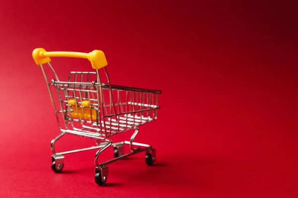 Gros plan du chariot d'épicerie de supermarché pour faire du shopping avec des roues noires et des éléments en plastique jaune sur poignée isolée sur fond rouge. Concept de shopping. Espace de copie pour la publicité — Photo