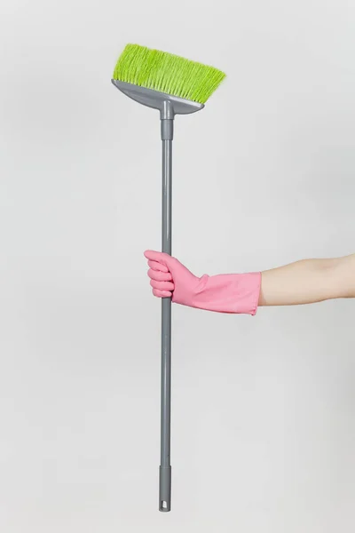 在粉红色的手套关闭女性手持有长灰色扫帚与绿色绒毛清洁和清扫在白色背景上隔离。清洁用品的概念。复制广告空间 — 图库照片