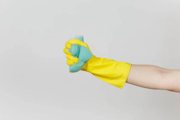 Il primo piano di mano femminile in guanti gialli tiene e stringe la grande spugna azzurra per pulire e lavare piatti isolati su sfondo bianco. Concetto di forniture di pulizia. Copia spazio per pubblicità — Foto Stock