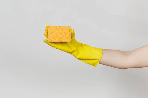 Close up de mão feminina em luvas amarelas horizontal detém esponja amarelo-laranja para a limpeza e lavagem de pratos isolados em fundo branco. Conceito de material de limpeza. Espaço de cópia para propaganda — Fotografia de Stock