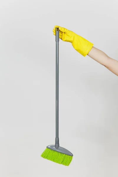 在黄色手套关闭女性手持有长灰色扫帚与绿色绒毛清洁和清扫在白色背景上隔离。清洁用品的概念。复制广告空间 — 图库照片