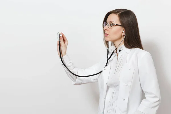 Concentrated confident experienced beautiful young doctor woman using stethoscope isolated on white background. Female doctor in medical gown glasses. Healthcare personnel, health, medicine concept.