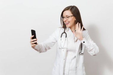 Eğlence gülümseyen güzel genç doktor kadın stetoskop, beyaz arka plan üzerinde izole gözlük ile. Kadın doktor tıbbi elbise üstünde hareket eden telefon selfie yapıyor. Sağlık personeli, sağlık, tıp konsantrasyon