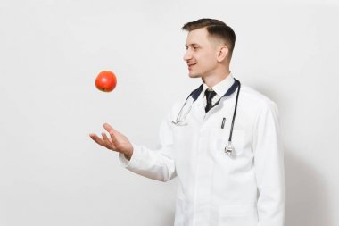Beyaz arka plan üzerinde izole gülümseyen genç doktor adam. Kırmızı elma kadar atma tıbbi üniforma, stetoskop erkek doktor. Sağlık personeli, sağlık, tıp kavramı. Doğru beslenme. Kopya alanı.