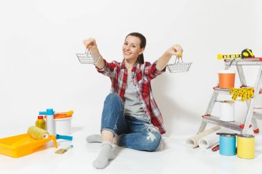 Kadın metal bakkal alışveriş sepetleri tutar, beyaz arka plan üzerinde izole yenileme daire için aygıtlar ile katta oturuyor. Duvar kağıdı, aksesuarlar, resim için araçlar. Onarım ev concept.