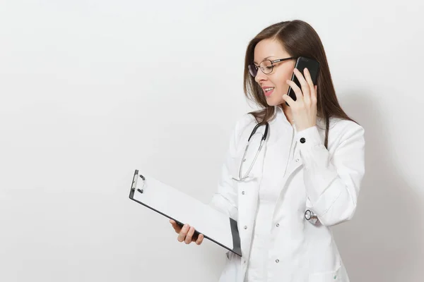 Jovem doutora sorridente com estetoscópio, óculos isolados sobre fundo branco. Médica feminina em vestido médico falar no telefone celular, mantenha o cartão de saúde na pasta notepad. Conceito de pessoal de saúde . — Fotografia de Stock