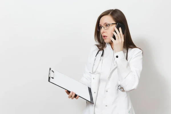 Mulher médica jovem grave com estetoscópio, óculos isolados em fundo branco. Médica feminina em vestido médico falar no telefone celular, mantenha o cartão de saúde na pasta notepad. Conceito de pessoal de saúde . — Fotografia de Stock