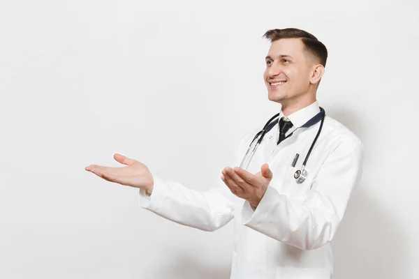 Sorridente felice giovane medico isolato su sfondo bianco. Medico maschio in uniforme medica, stetoscopio guardando da parte, allargando le mani per il saluto. Personale sanitario, salute, concetto di medicina . — Foto Stock