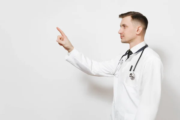 Серйозний молодий лікар ізольований на білому тлі. Чоловік-лікар у медичній сукні, стетоскоп торкається чогось на кшталт натискання кнопки, натискає на місце для копіювання. Медичний персонал, охорона здоров'я, концепція медицини — стокове фото