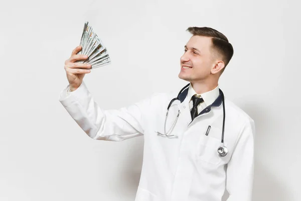 Un jeune médecin souriant isolé sur fond blanc. Médecin en uniforme médical, stéthoscope avec un paquet de dollars, billets de banque, argent comptant. Personnel de santé, santé, concept de médecine . — Photo
