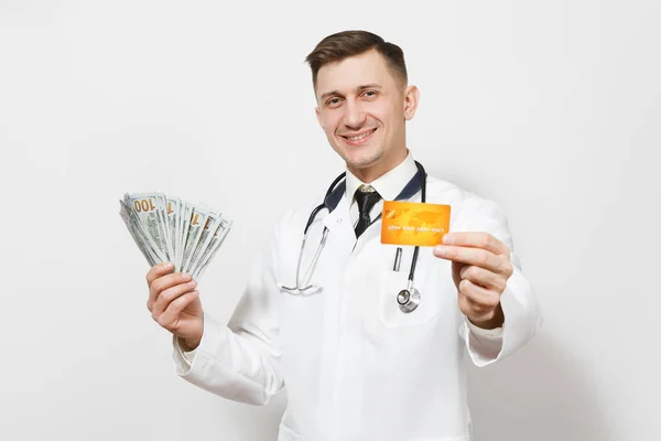 Усміхнений молодий лікар ізольований на білому тлі. Чоловік-лікар в медичній формі, стетоскоп тримає пакет доларів, банкноти готівкові гроші, кредитну картку. Медичний персонал, концепція медицини . — стокове фото