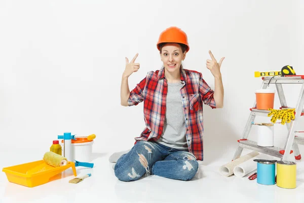 Mujer loca divertida en casco protector naranja sentado en el suelo con instrumentos para apartamento de renovación aislado sobre fondo blanco. Fondos de pantalla, accesorios para pegar, herramientas de pintura. Concepto de reparación . — Foto de Stock
