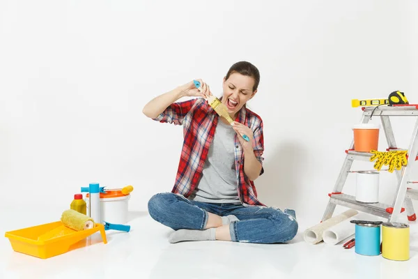 Διασκεδαστικό γυναίκα σε casual ρούχα που κάθεται στο πάτωμα με πινέλο, όργανα για ανακαίνιση Διαμέρισμα Δωμάτιο απομονωθεί σε λευκό φόντο. Ταπετσαρία, αξεσουάρ για την κόλληση, εργαλεία ζωγραφικής. Επισκευή concept home. — Φωτογραφία Αρχείου